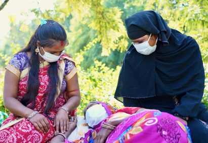 A closeup of three Indian women with one of them lying down, all wearing facemask during daylight