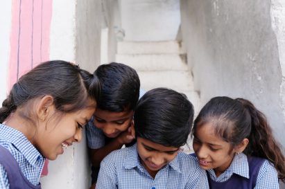 A group of smiling Indian school children in uniforms looking down at something at school